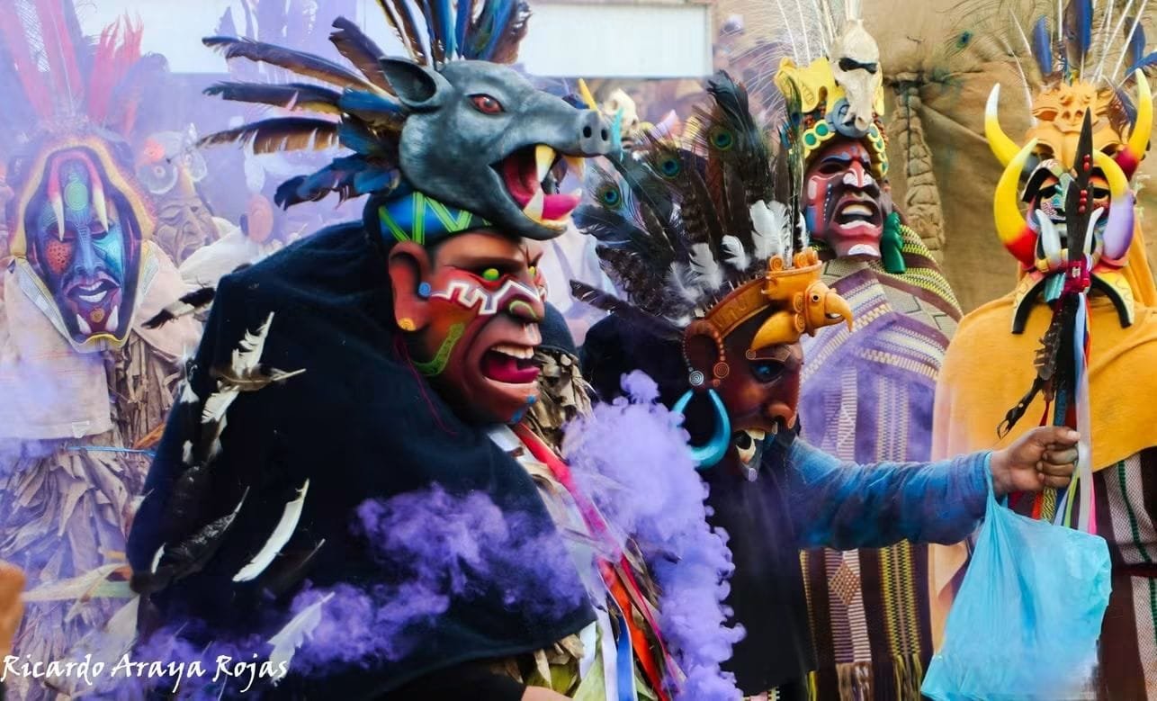 Primer plano de máscaras pintadas con plumas y colmillos, rodeadas de humo morado