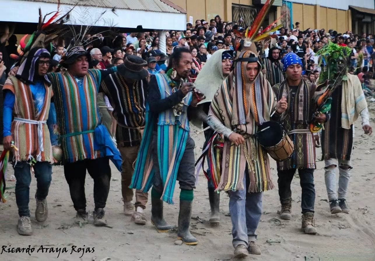 Músicos con ponchos tejidos a rayas tocan tambor y flauta mientras caminan frente al público